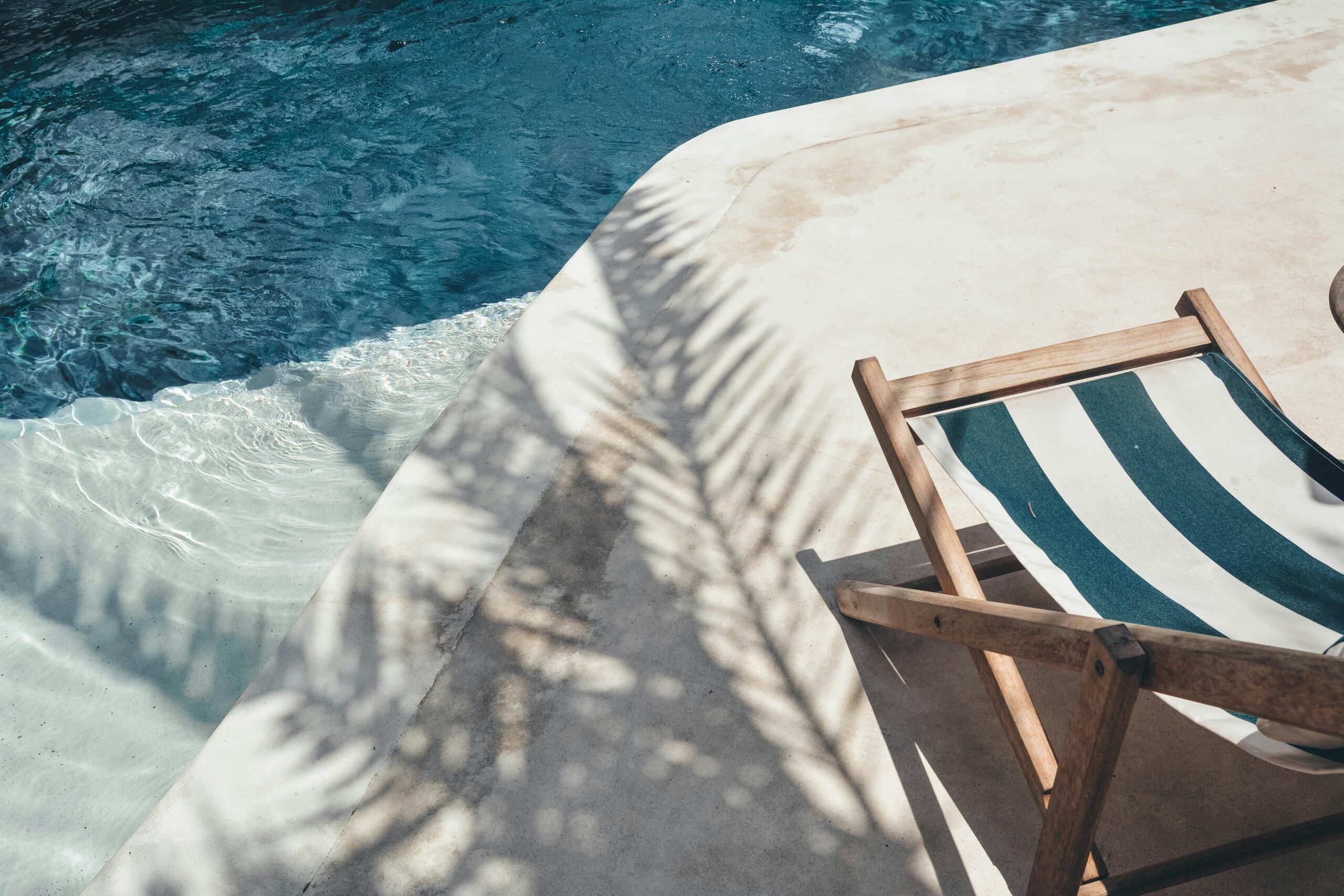 Serene poolside lounger with palm shadows, perfect for summer relaxation in Bali.
